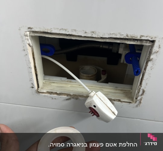 יד מחזיקה טבעת פלסטיק מול קיר עם חור צנרת